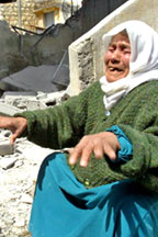 Une vieille femme voilée lève les mains en signe d'angoisse devant les ruines d'une maison