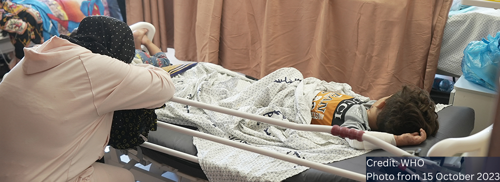 Women with her head in her hands leaning over a hospital bed on which a child is laying.