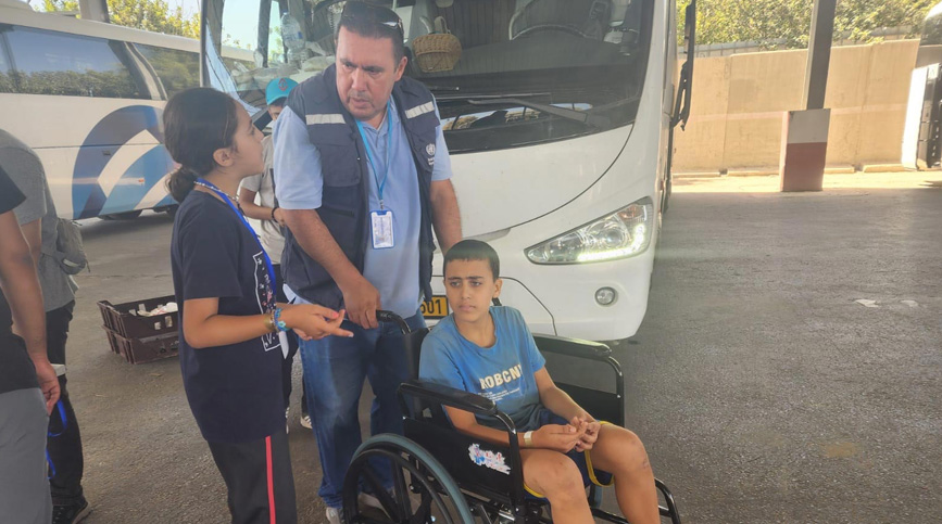 Health workers assist children at a border transit point, offering support and care for those in need, including a young boy in a wheelchair, as part of ongoing humanitarian efforts