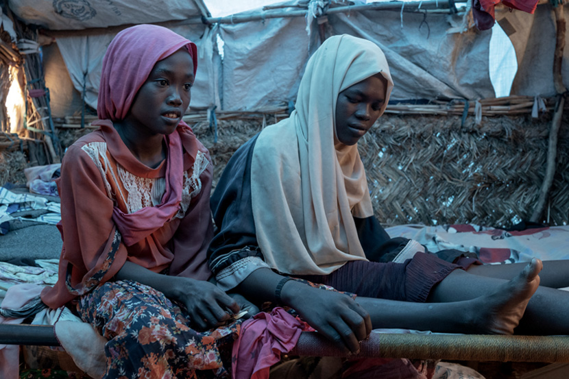 Aliya Noor’s elder daughters, Mayad, 12, and Salima, 15, sit on a bed inside the makeshift home they built in the refugee camp in Adre, Chad. Photo: WHO / Nicolò Filippo Rosso 